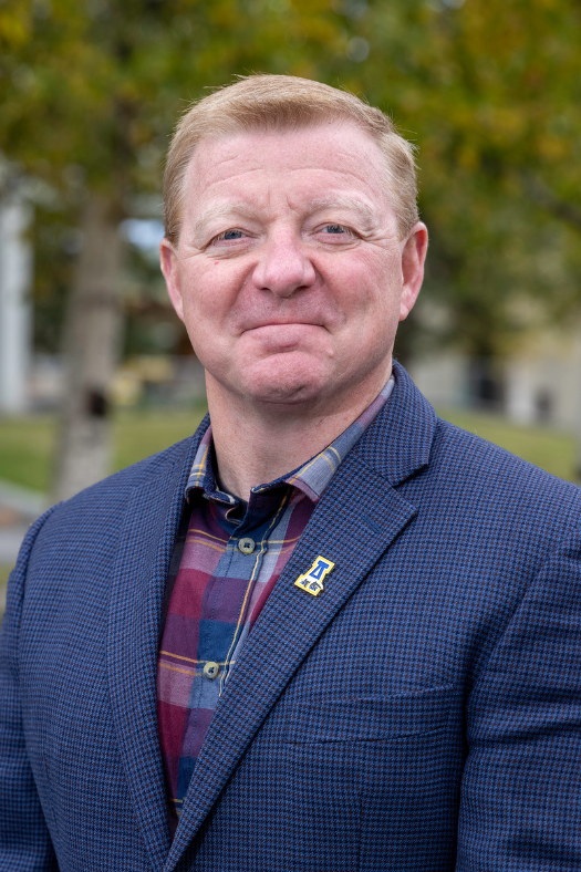 Portrait of Tom Hough, in a suit, on a summer UAF campus