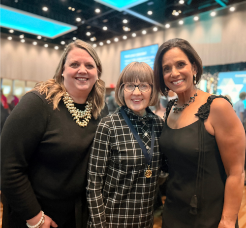 three women pose together at a formal event