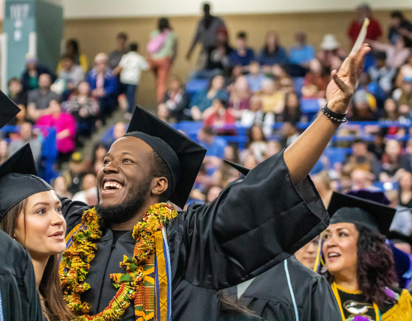 a male grad waves at his family in the stands