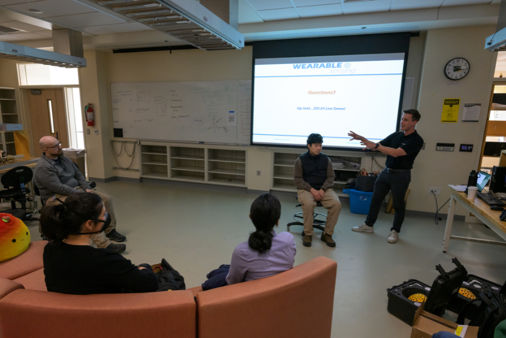 a man points to the projection screen as students look on