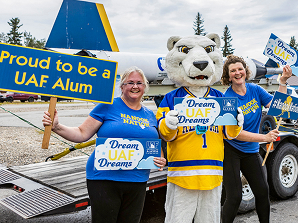 Two people dressed in blue and gold and the polar bear mascot pose with signs in a parade