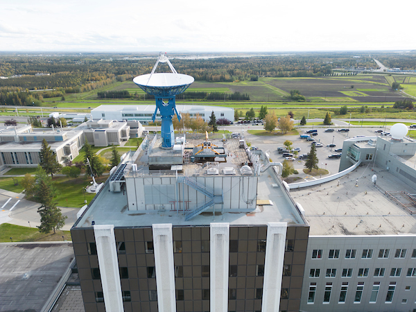 Drone photo above a brown campus building overlooking a summer scene and blue sky