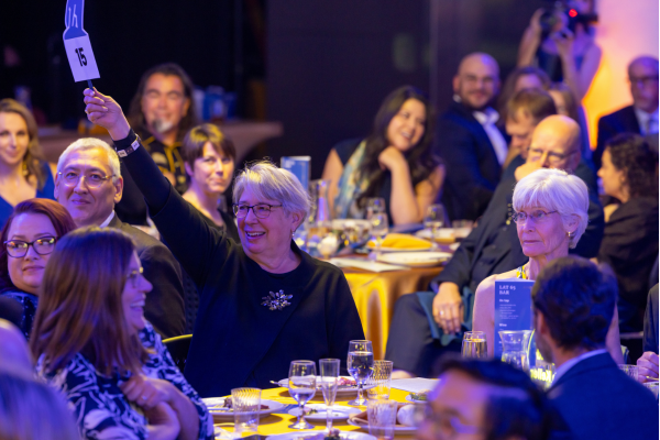 A woman holds an auction paddle above her head at a full table