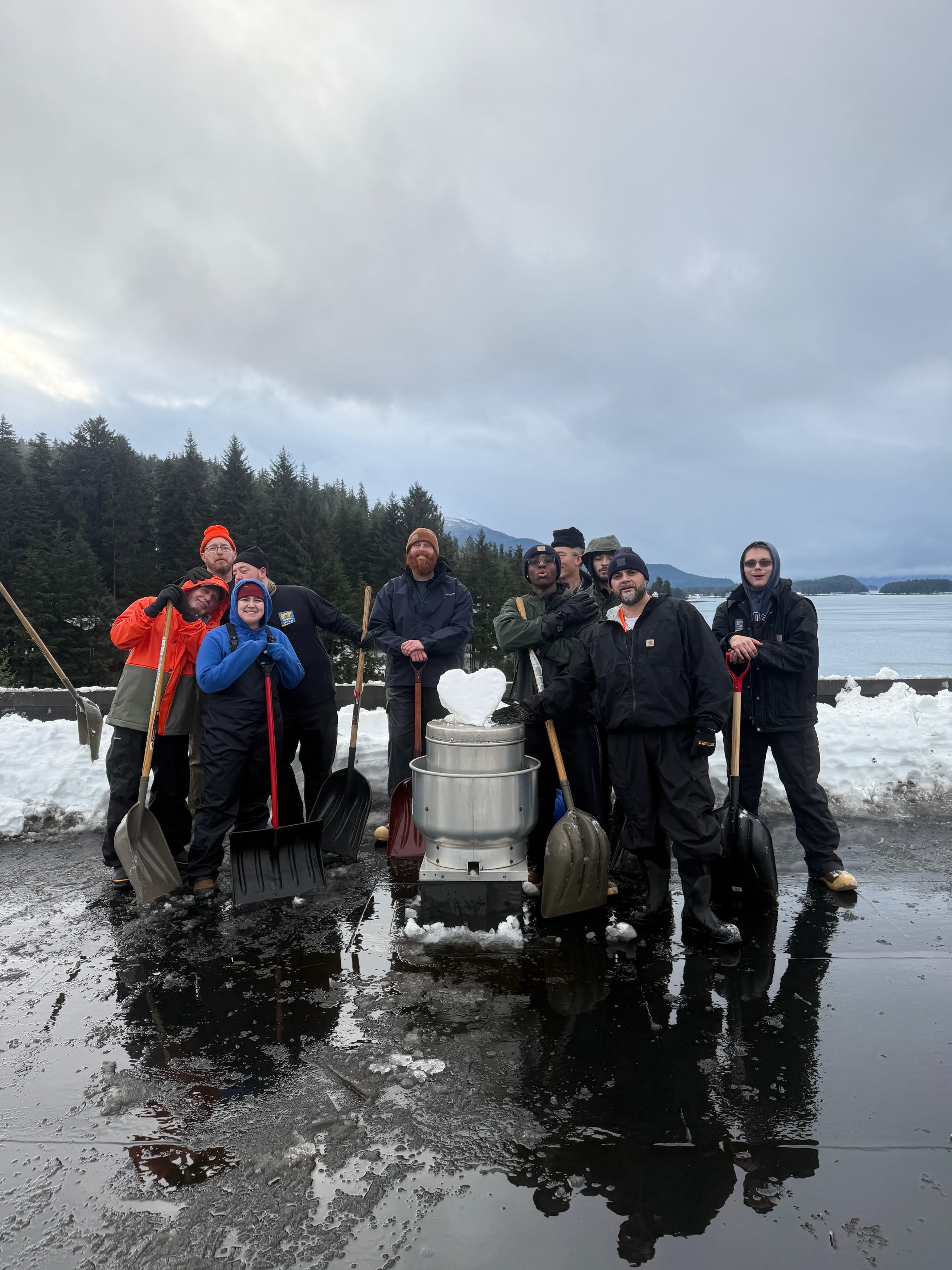 A group of people with shovels stand on a roof around a heart made from snow.