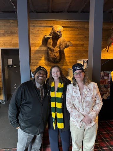 three people stand together with stuffed grizzly bear behind them