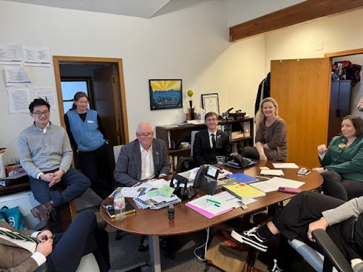 a group of people sit and stand around a round table in an office 