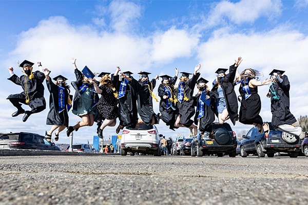 A group of graduates in regalia leap in a posed photo