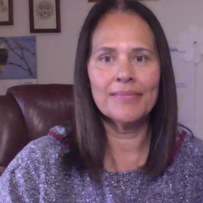 A woman with long dark hair sits in a desk chair