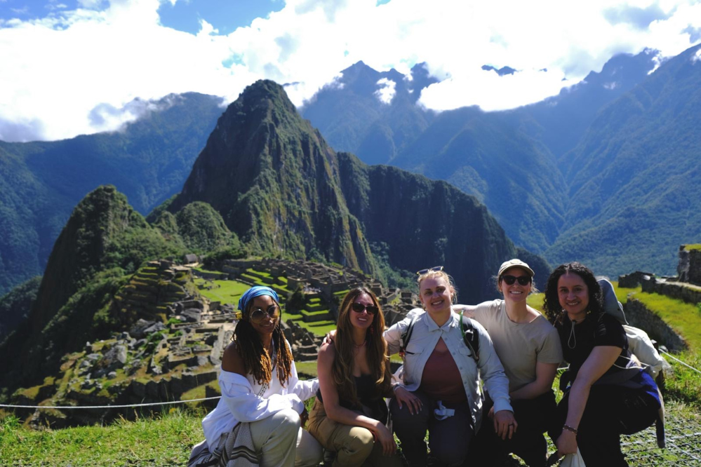 five woman crouch together with Machu Pichu in the background