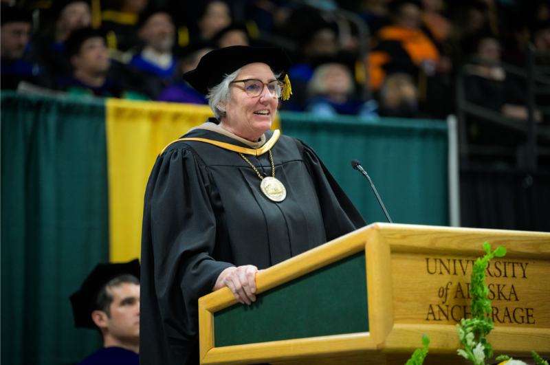 President Pitney stands at the wooden and green podium in graduation regalia