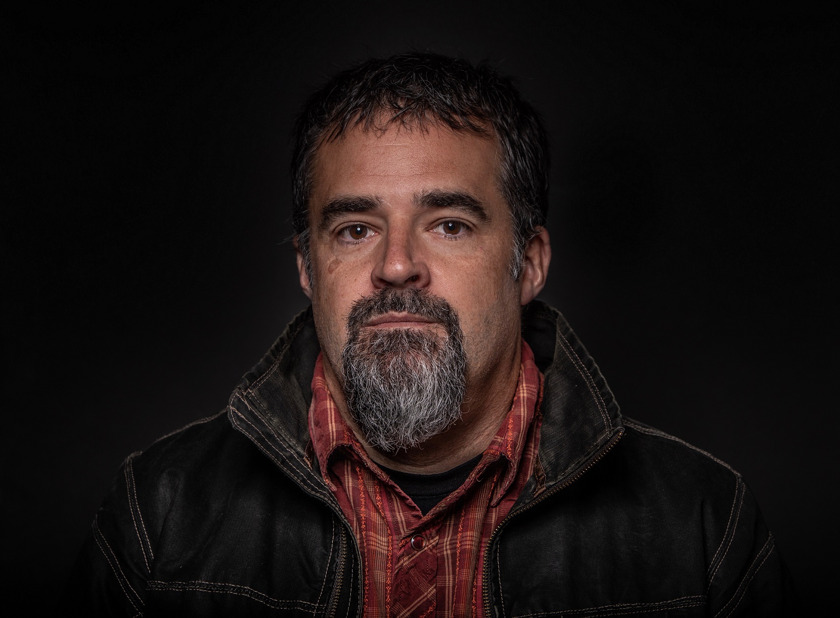 a man with short hair and large jacket with black background