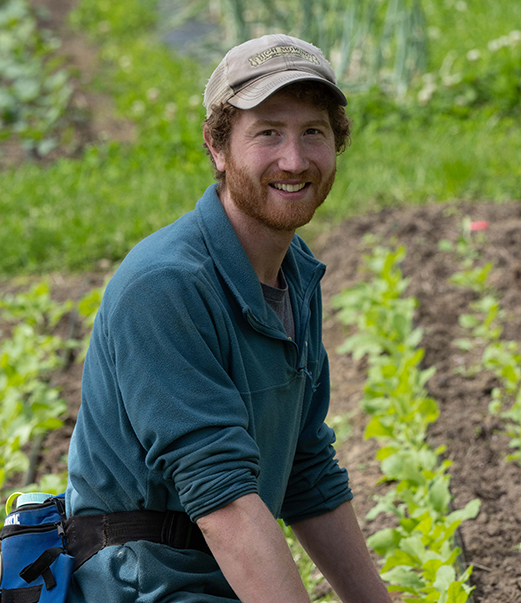 A man with a hat leans over a plot in an outdoor garden.