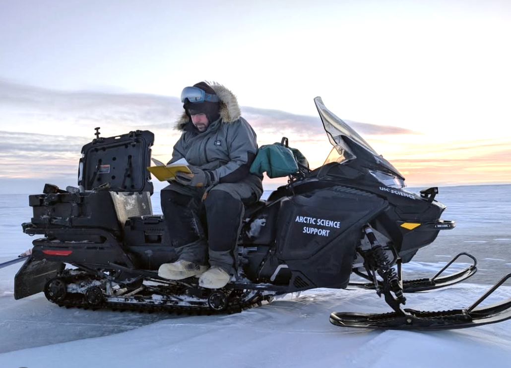 a man in winter gear sits and writes on a black snowmachine