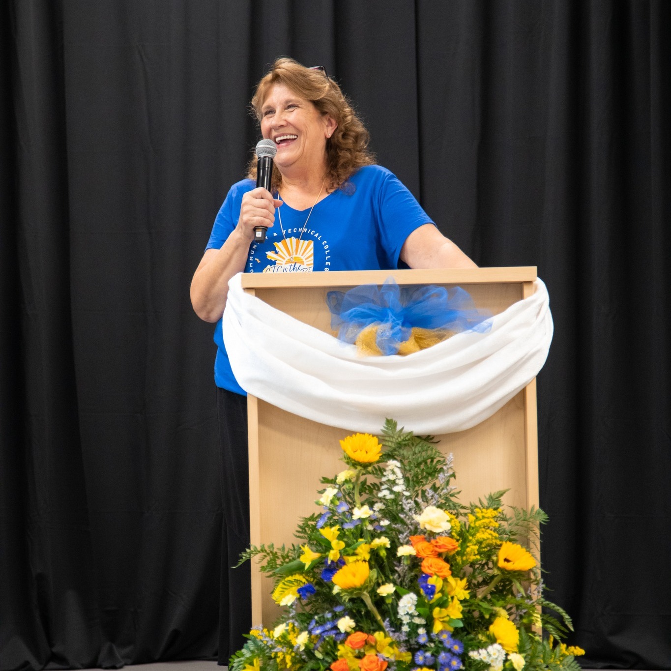 Stalder stands at a podium with a microphone during her farewell ceremony