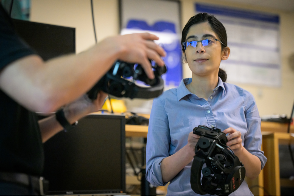 A researcher holds a black DSI-24 EEG headset while another person, partly visible in the foreground, holds a second headset.