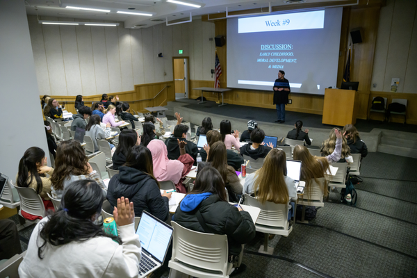 A group of students sit in a lecture hall as the professor stands in front
