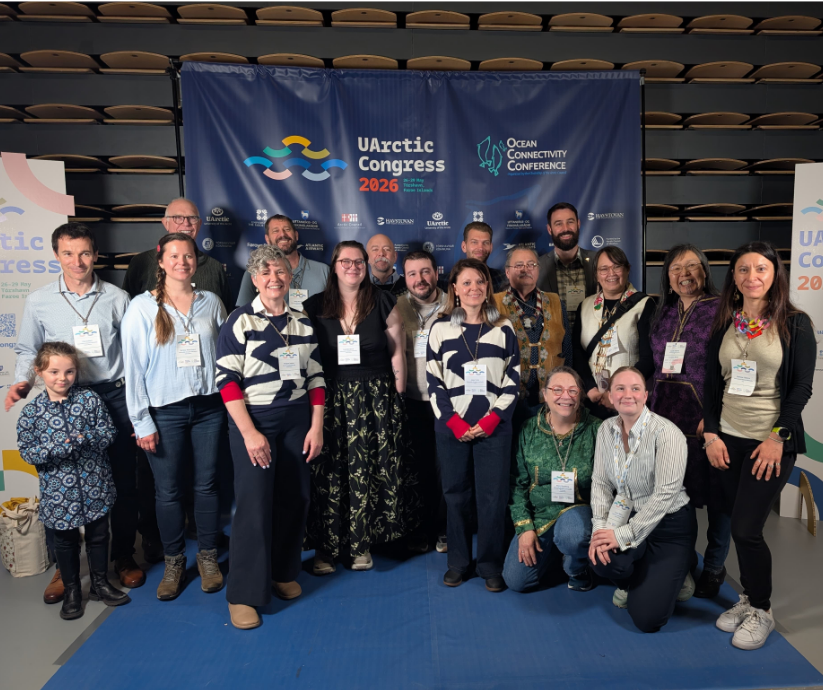 A group of roughly 18 people stand in front of a UArctic Congress 2026 and Ocean Connectivity Conference banner inside a large venue in Tórshavn, Faroe Islands. All are wearing conference lanyards and badges.