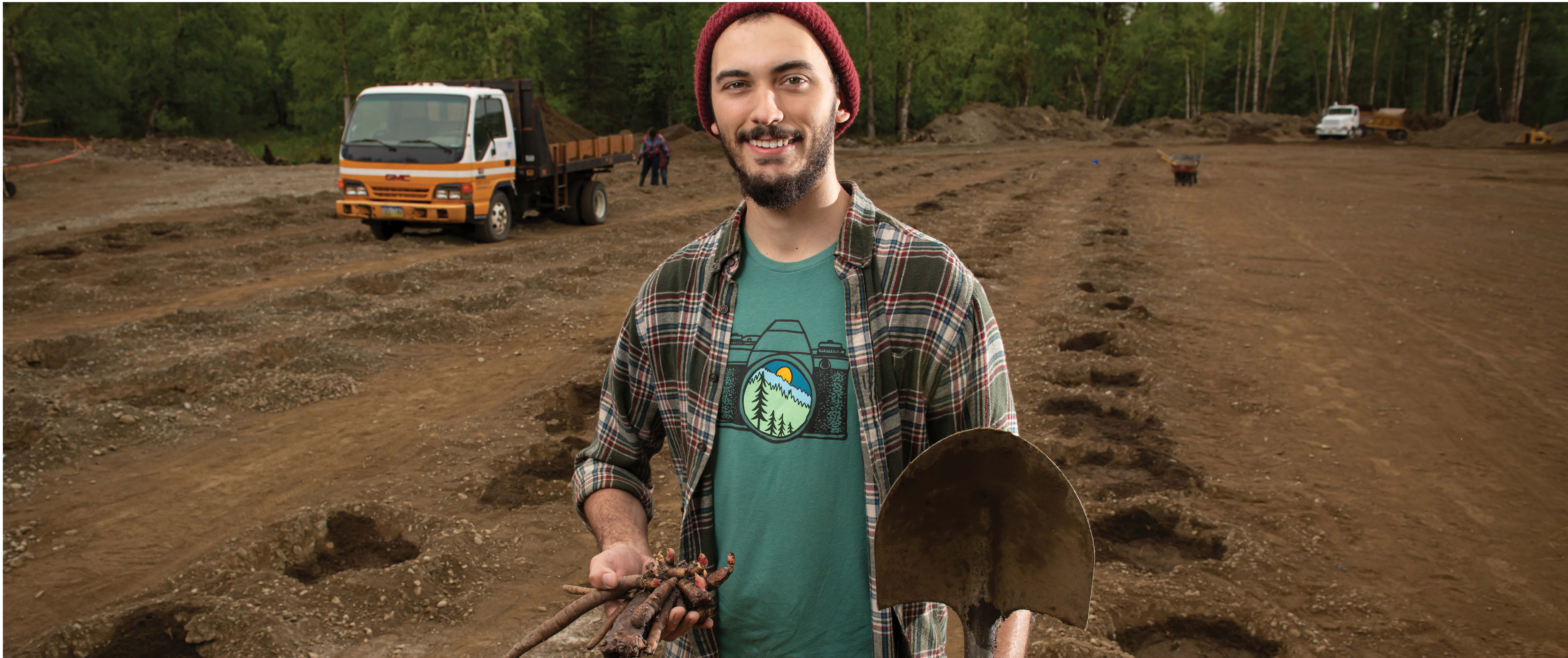 Student on a farming field holding a shovel