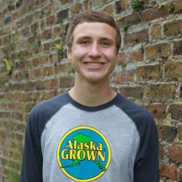 Luke Rogers stands in front of a brick wall, smiling at the camera